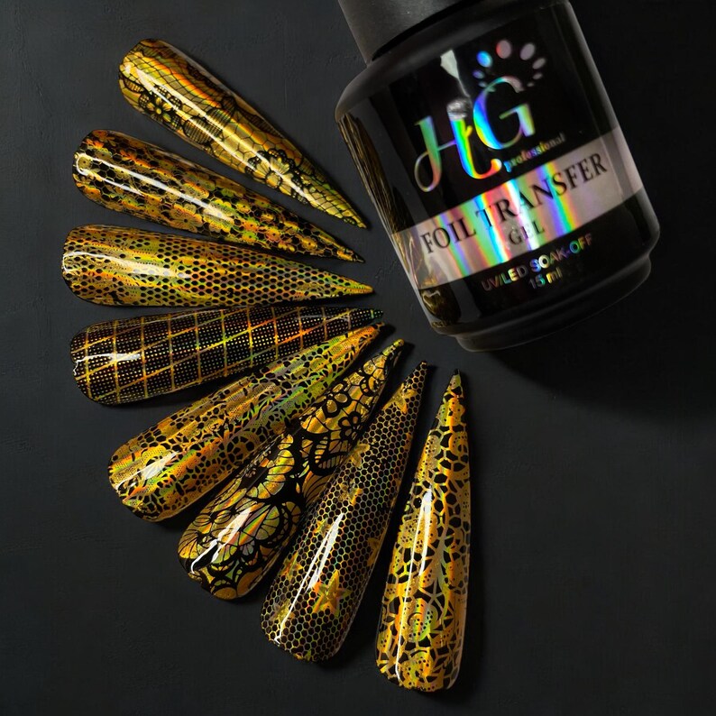 Op de afbeelding: Een fles HG Professional Foil Transfer Gel, een heldere gel met een zwart etiket en zilveren letters. De fles is omringd door tien nageltips met verschillende gouden folieontwerpen.