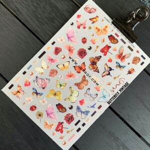 Puede incluir: Una hoja de pegatinas de u&ntilde;as de mariposa de colores sobre un fondo blanco. Las pegatinas presentan mariposas de varios colores, incluyendo rosa, azul, amarillo, naranja y verde. La hoja tambi&eacute;n incluye peque&ntilde;as flores, perlas y una mariquita. El texto "www.hgprof.com" y "butterfly_vintage" est&aacute; impreso en la hoja.