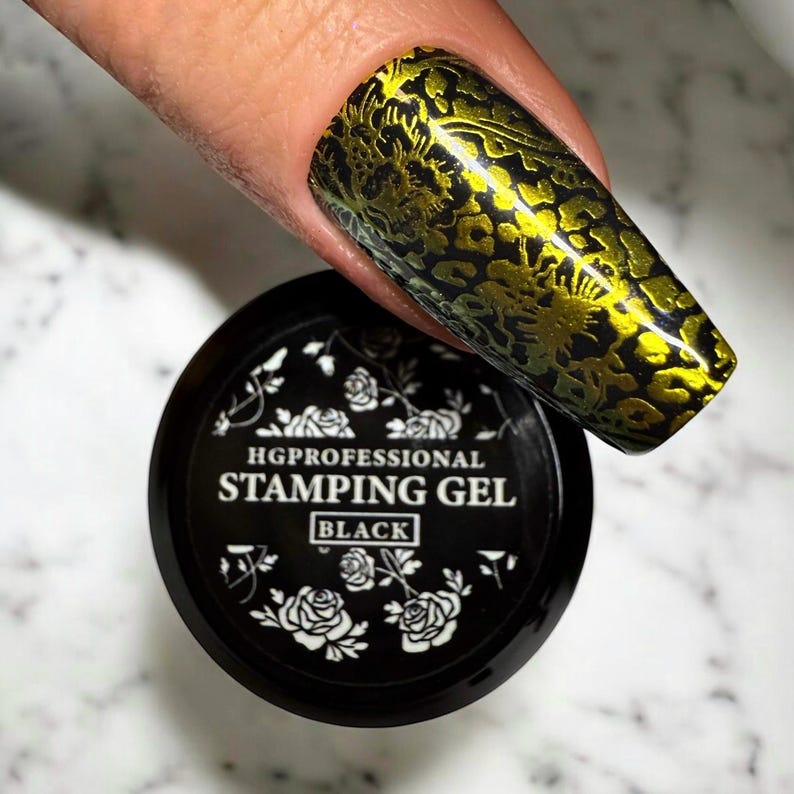 May include: A black jar of HG Professional stamping gel with white floral designs and the text "HG Professional Stamping Gel Black". A fingernail with a gold and black nail design is visible in the background.