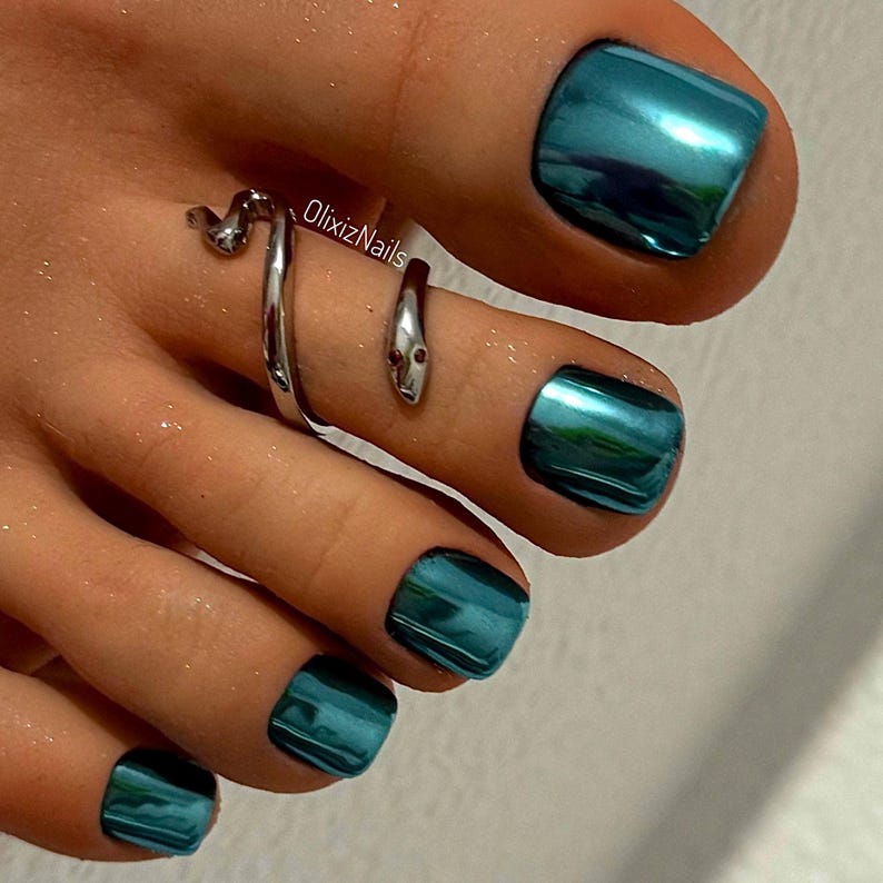 May include: Close-up of a foot with teal metallic nail polish and a silver snake toe ring. The nail polish has a glossy finish. The toe ring wraps around the toe with a snake head design. The text "OlixizNails" is visible.