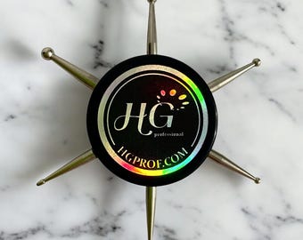 May include: A set of six silver nail art tools with rounded tips, arranged in a star shape around a black circular base with a holographic sticker featuring the logo "HG professional" and the website "HGPROF.COM".