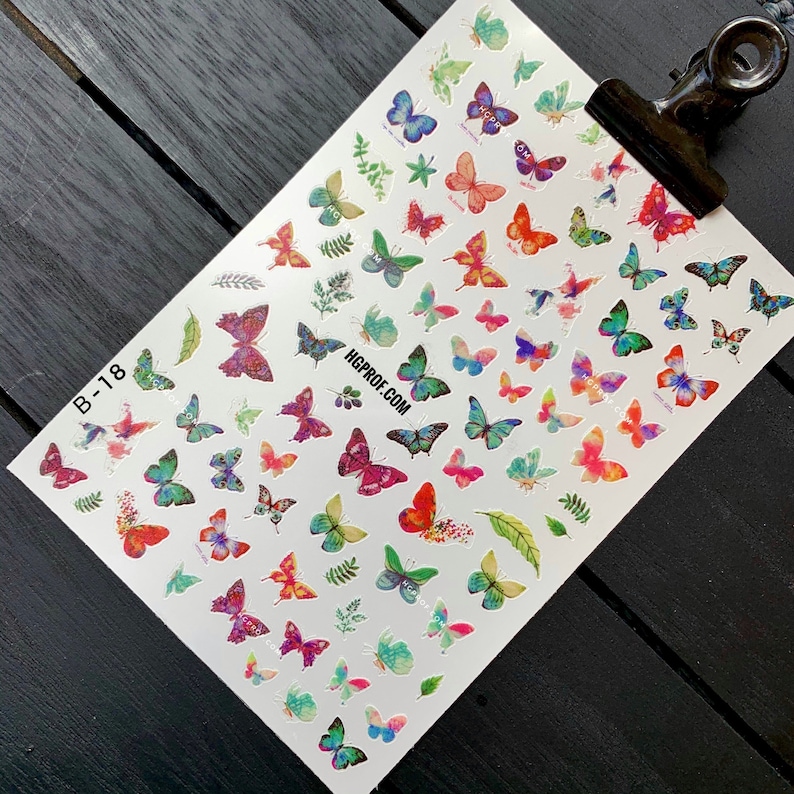 Puede incluir: Una hoja de pegatinas de u&ntilde;as con forma de mariposa de colores vivos sobre un fondo blanco. Las pegatinas presentan una variedad de dise&ntilde;os de mariposas en tonos de rosa, azul, verde y morado. La hoja tambi&eacute;n incluye peque&ntilde;as hojas verdes. El texto "HGPROF.COM" est&aacute; impreso en el centro de la hoja.