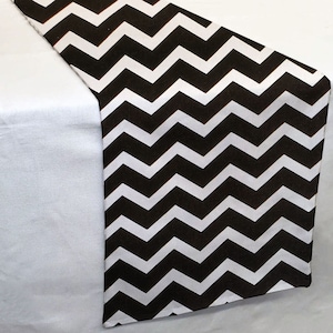 May include: Black and white chevron table runner. The runner has a repeating pattern of white and black zigzags.