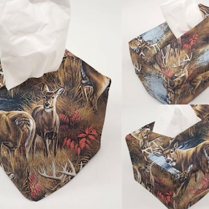 May include: A set of three decorative tissue box covers. Each cover features a woodland scene with deer, antlers, and foliage in shades of brown, green, and red. White tissues are visible in the openings.