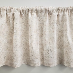 May include: A valance curtain with a cream-colored background and a pattern of small, scattered brown dots. The fabric is gathered at the top, creating soft folds. The bottom edge has a gentle, scalloped shape.