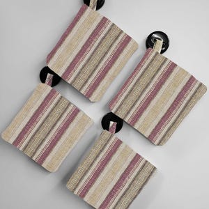 May include: Four striped fabric pot holders with black button closures. The pot holders are beige with pink and brown stripes.