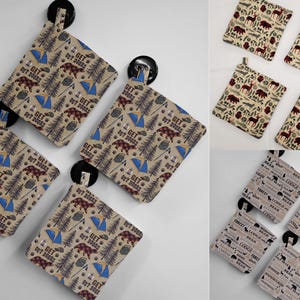May include: A collection of square pot holders with various outdoor-themed patterns. Designs include bears, trees, tents, and the text "GET OUT DOORS". The pot holders are in shades of tan, brown, and blue, perfect for a rustic kitchen.