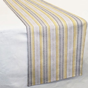 May include: A yellow and gray striped table runner. The runner is made of a woven fabric and has a subtle texture.