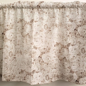May include: A valance curtain featuring a repeating pattern of white and light brown roses. The fabric is gathered at the top, creating soft folds. The floral design gives a romantic and classic feel, suitable for a bedroom or living room.