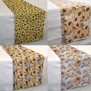 May include: Four different table runners with fall-themed designs. The runners feature sunflowers, pumpkins, and birds. The runners are all made of fabric and have a rectangular shape.