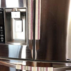 May include: Two sets of fabric refrigerator handle covers in a beige and burgundy striped pattern. The covers are attached to the handles of a stainless steel refrigerator.