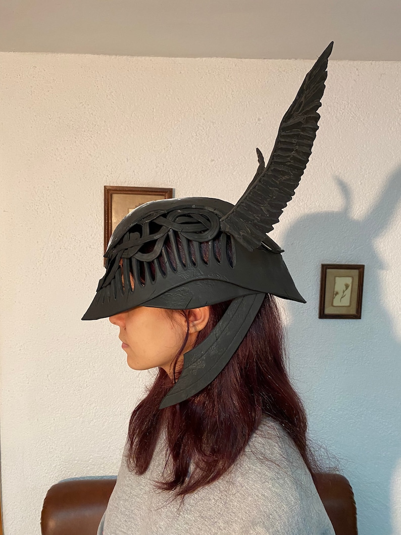 May include: A black helmet with a wing design on the side. The helmet has a detailed, intricate design and appears to be made of a hard material.