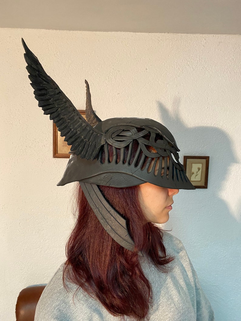 May include: A black helmet with a winged design and a detailed, intricate pattern. The helmet has a long, pointed horn on the top and a wide brim.