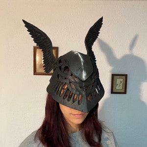 May include: A black, 3D printed helmet with intricate details and wings. The helmet is made of a lightweight material and has a unique design.
