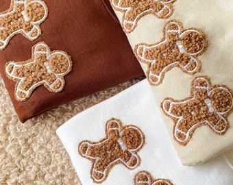 May include: Two sweatshirts with gingerbread man embroidery. One sweatshirt is brown with three gingerbread men and the other is white with five gingerbread men.