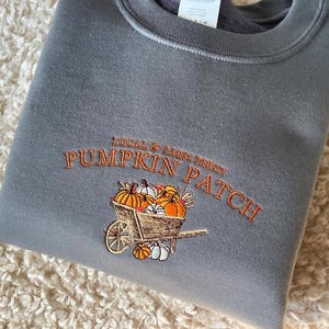 Embroidered sweatshirt with a Pumpkin Patch design, featuring pumpkins in a wagon with some autumn leaves on a charcoal sweater.