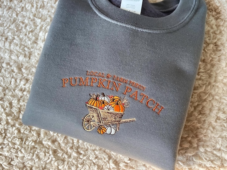 Embroidered sweatshirt with a Pumpkin Patch design, featuring pumpkins in a wagon with some autumn leaves on a charcoal sweater.