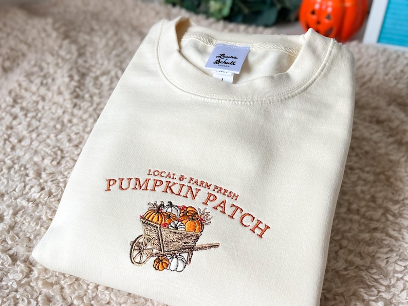 Embroidered sweatshirt with a Pumpkin Patch design, featuring pumpkins in a wagon with some autumn leaves on a cream sweater.