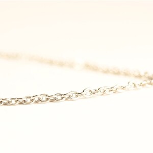 May include: A silver-colored chain necklace with a series of small, rounded links. The chain is displayed against a white background, with the focus on the chain's texture and design. The necklace is a simple, elegant piece of jewelry.