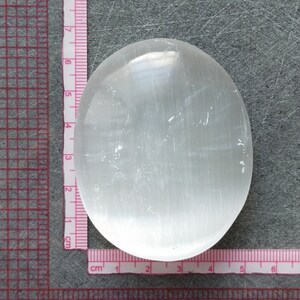 May include: A smooth, white selenite palm stone with a slightly oval shape. The stone is approximately 5 cm in diameter.