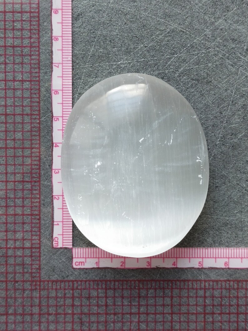 May include: A smooth, white selenite palm stone with a slightly oval shape. The stone is approximately 5 cm in diameter.