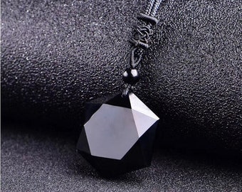 Puede incluir: Un colgante de obsidiana negra en forma de estrella de siete puntas, colgado de un cordón negro.