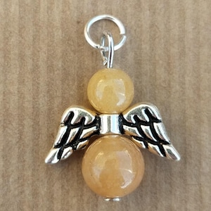 Peut inclure: Un charme d'ange en argent avec deux perles de pierre précieuse jaune-orange. L'ange a des ailes et une auréole.