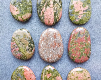Op de afbeelding: Tien gladde, ovale stenen met een groen, roze en wit marmerpatroon. De stenen zijn in drie rijen op een grijze achtergrond gerangschikt.