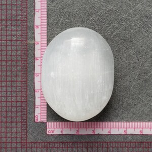 May include: A white selenite crystal palm stone, approximately 4 cm in diameter, with a smooth, polished surface and visible striations.