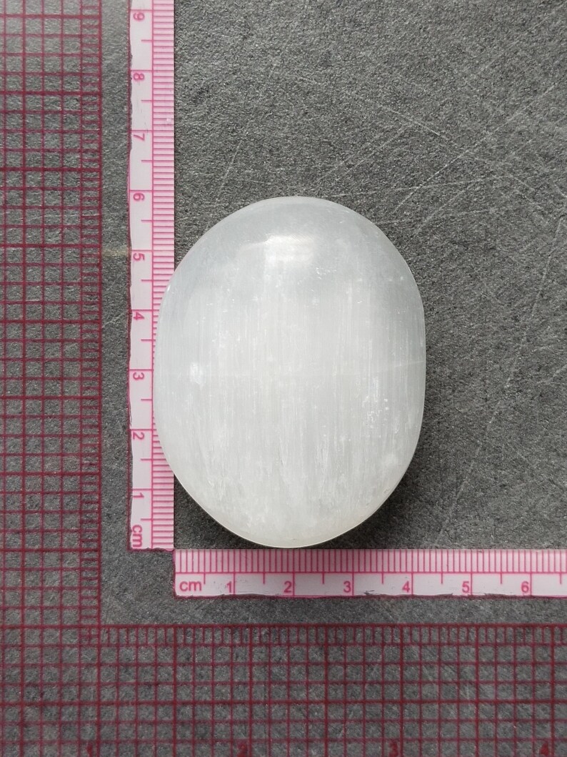 May include: A white selenite crystal palm stone, approximately 4 cm in diameter, with a smooth, polished surface and visible striations.