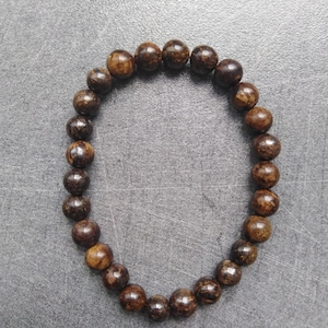 Peut inclure: Un bracelet en perles brunes avec une couleur brun foncé. Les perles sont rondes et ont une surface légèrement texturée.
