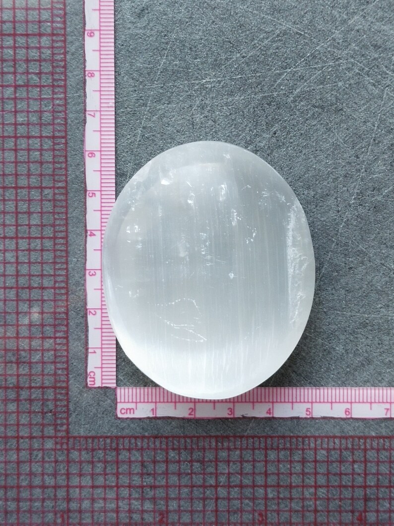 May include: A white selenite palm stone with a smooth, polished surface and visible striations. The stone is approximately 5 cm in diameter.