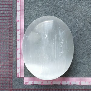 May include: A white selenite crystal slab, approximately 6 cm in diameter, with a smooth, polished surface. The crystal is translucent and has a slightly cloudy appearance.