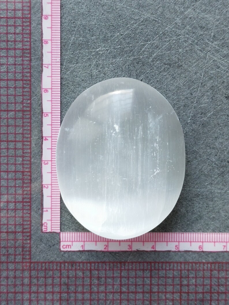 May include: A white selenite crystal slab, approximately 6 cm in diameter, with a smooth, polished surface. The crystal is translucent and has a slightly cloudy appearance.