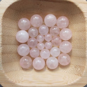 Peut inclure: Un ensemble de perles de quartz rose de couleur rose dans un bol en bois. Les perles sont lisses et rondes, et elles sont toutes de la même taille.