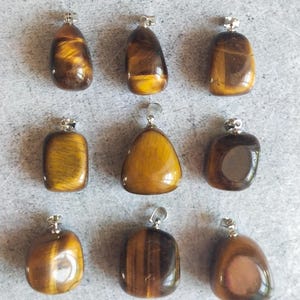Peut inclure: Neuf pendentifs en œil de tigre polis, avec des bélières argentées. Les pendentifs de formes variées présentent les motifs naturels bruns et dorés de la pierre. Chaque pendentif est unique, avec des variations de couleur et de motif.