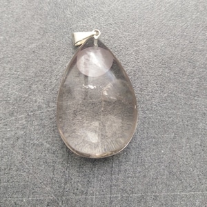 Peut inclure: Un pendentif en forme de larme en quartz clair avec une bélière en argent. Le quartz a un aspect nuageux, laiteux avec une petite inclusion ronde rose au centre.