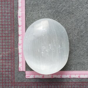 May include: A white selenite crystal palm stone, measuring approximately 5 cm in diameter. The stone has a smooth, polished surface with visible striations.