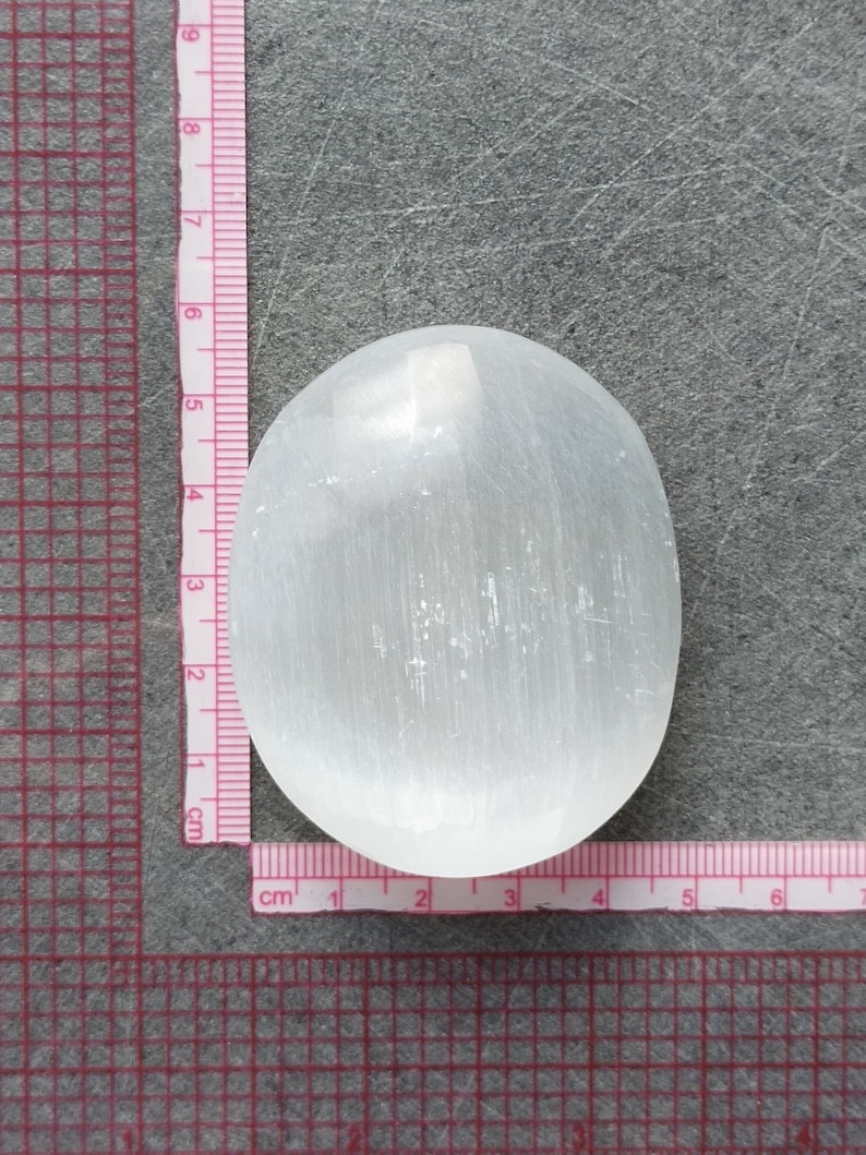 May include: A white selenite crystal palm stone, measuring approximately 5 cm in diameter. The stone has a smooth, polished surface with visible striations.