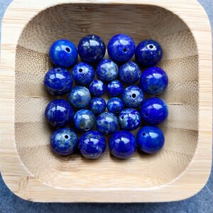 Peut inclure: Un bol en bois contenant une collection de perles rondes en lapis-lazuli bleu. Les perles sont lisses et polies.