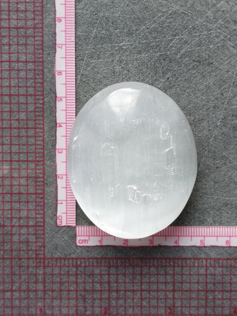 May include: A white selenite palm stone, approximately 5 cm in diameter, with a smooth, polished surface. The stone has a natural, cloudy appearance with subtle striations.