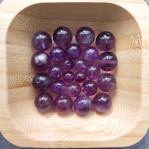 Peut inclure: Un bol rempli de perles de pierres précieuses d'améthyste. Les perles sont rondes et polies, d'une couleur violet foncé.