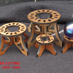 May include: Four wooden stands of varying sizes with intricate laser-cut designs. The stands are made of light brown wood with a darker brown stain. A iridescent glass orb sits on the smallest stand.