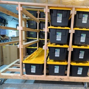 May include: A wooden storage rack with wheels, holding multiple black and yellow storage bins. The rack is made of unfinished wood and has a simple design.