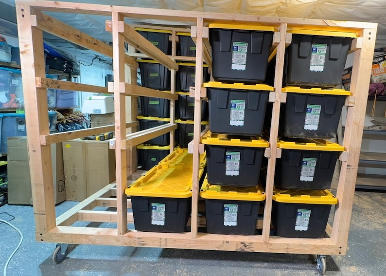 May include: A wooden storage rack with wheels, holding multiple black and yellow storage bins. The rack is made of unfinished wood and has a simple design.
