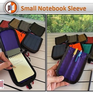 May include: A small notebook sleeve in purple with a black zipper and a red pull tab. The sleeve is open and a small notebook with a spiral binding is inside. The notebook has yellow lined paper and the words "Pocket Designs Rule" are written on the first page. The sleeve is made in the USA.