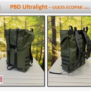 May include: A green backpack with black straps and a black label that says "PBD Ultralight - ULK35 ECOPAK EPK200". The backpack is sitting on a wooden table in front of a green forest background.