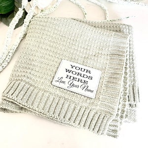 May include: A light green knitted throw blanket with a white square patch that says "YOUR WORDS HERE Love, Your Name".