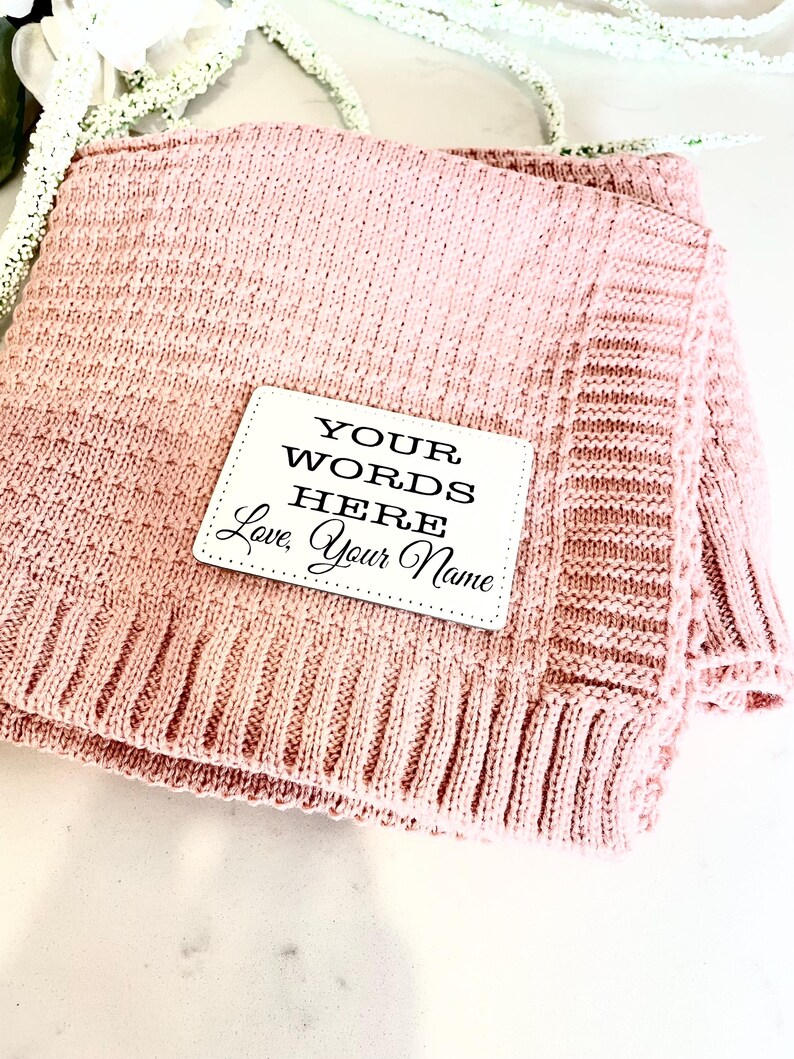 May include: A pink knitted blanket with a white tag that says "YOUR WORDS HERE, Love, Your Name".