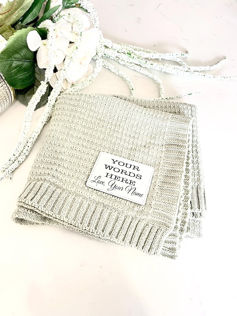 May include: A light green knitted throw blanket with a white square patch that says "YOUR WORDS HERE Love, Your Name".